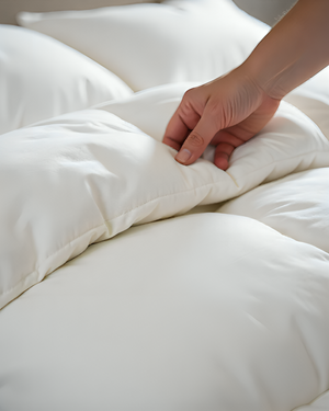 Hand touching a white comforter on a bed
